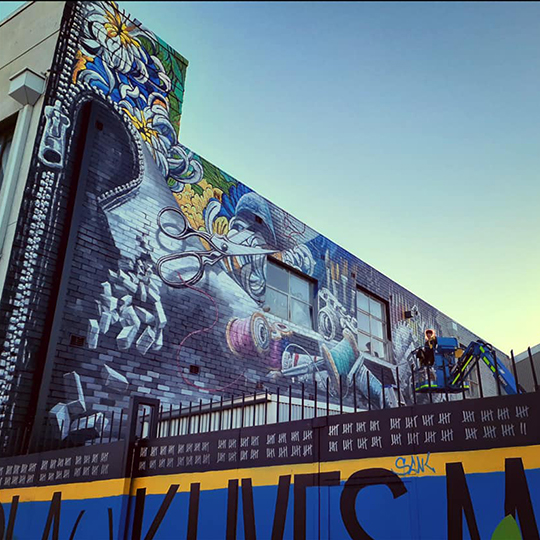 Artist Camilla Lawson paints a mural from a scissor lift